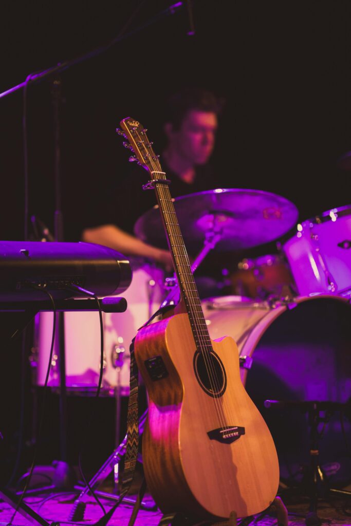 Close-up of a guitar on stage with a drummer in the background during a live performance.